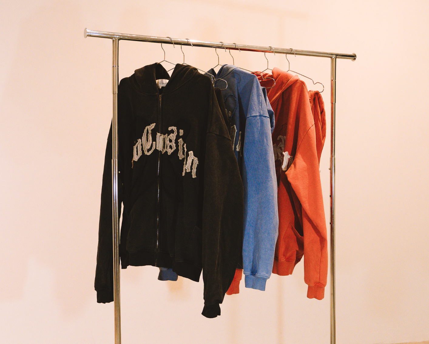 Clothing rack with hoodies on a beige floor and light pink wall